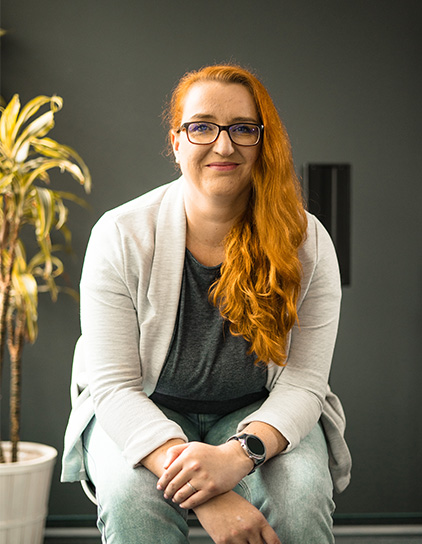 Evelyn Rodmann mit rotem Haar im Büro sitzend, Teamfoto