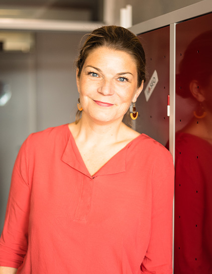 Hanna Sturm in rotem Pullover lehnt sich an einen Spind