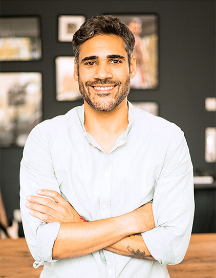 Portrait von Jonnie Klausch, sitzend und lächelnd auf einem braunen Ledersofa im Büro von Morefire