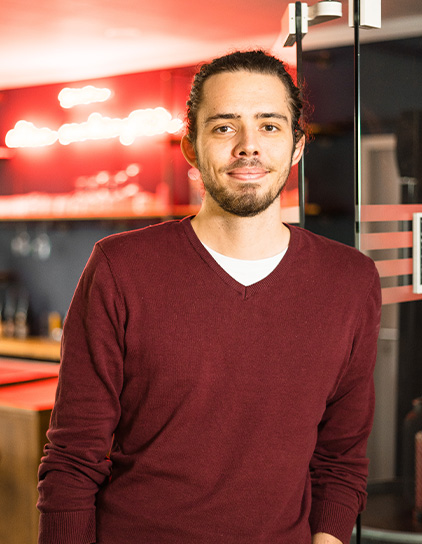 Portrait von Julian Klotz, lächelnd und vor einem Hintergrund mit Bar-Atmosphäre im Büro von Morefire