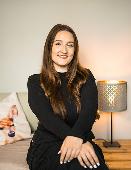 Laura Lüke, Mitarbeiterin, sitzt auf einem Sofa im Büro, im Hintergrund eine Lampe und ein Hundekissen