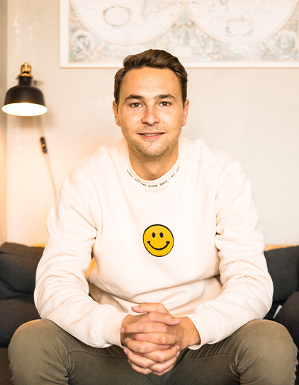 Lennert Laffin lächelt und trägt einen cremefarbenen Pullover mit einem Smiley