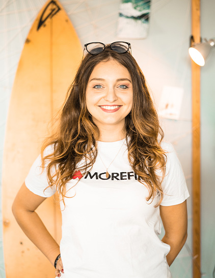 Lorena Simunovic trägt ein 'I Love Morefire' T-Shirt und steht vor einem Surfbrett