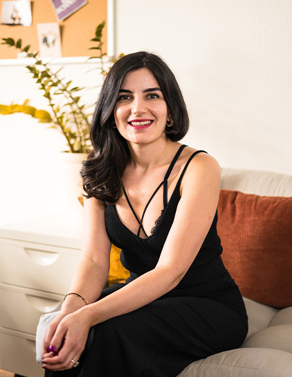 Mane Hovhannisyan trägt ein schwarzes Kleid, sitzt auf einem Sofa