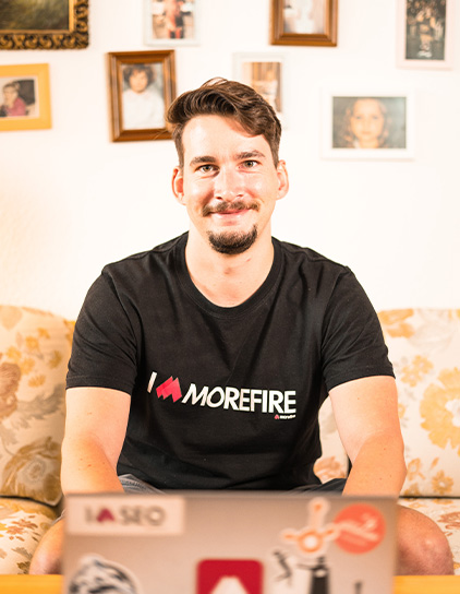 Patrick Graf in einem schwarzen T-Shirt, sitzt auf einem Sofa und lächelt in die Kamera