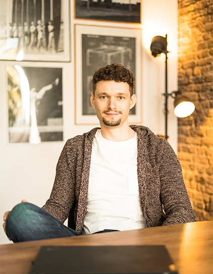 Patrick Pape in einem grauen Cardigan, sitzt am Tisch und lächelt in die Kamera