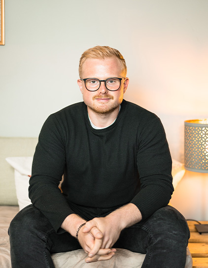 Robin Schmeing in einem schwarzen Pullover, sitzt und lächelt in die Kamera