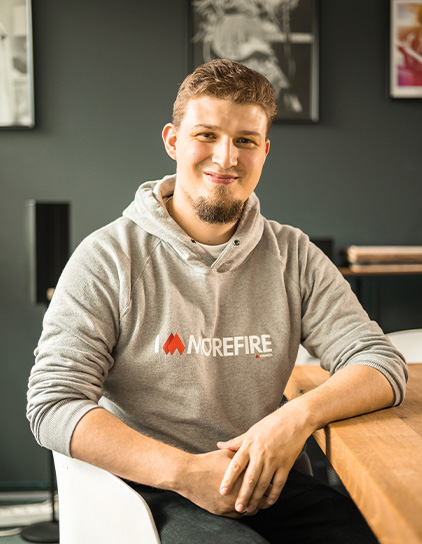 Sebastian Schnelting in einem grauen Hoodie mit 'Morefire'-Logo, lächelt in die Kamera