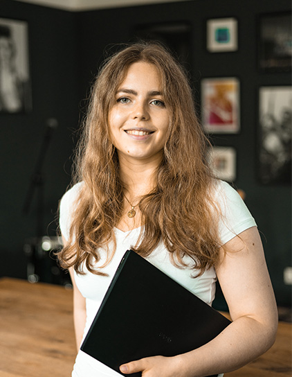 Sylvia Rinke in einem weißen T-Shirt, hält einen Laptop und lächelt in die Kamera