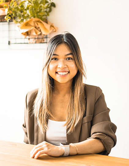Tanita Vi Anh Do in einem braunen Blazer, sitzt und lächelt in die Kamera