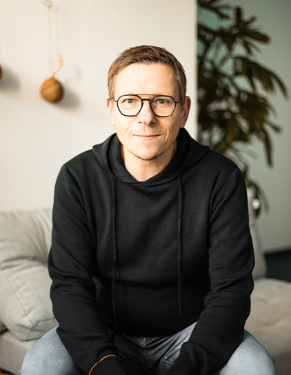 Thomas Waniek in einem schwarzen Kapuzenpullover, lächelt in die Kamera