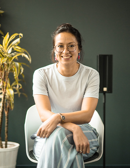 Veronique Hahn in einem grauen Hemd, sitzt und lächelt in die Kamera